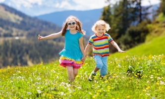 Mädchen und Junge laufen glücklich über Bergwiese im Sommer 