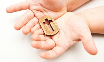 Kinderhände halten kleines Kreuz aus Holz 