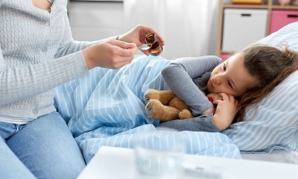 Kind liegt krank im Bett, Mutter gibt ihm Medizin