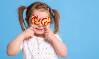 Kleines Mädchen hält sich zwei rot-gelb geringelte Lutscher vor die Augen 