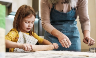 Mädchen rollt mit Oma Teig aus