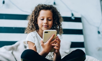 Mädchen sitzt auf Bett und schaut konzentriert aufs Smartphone 