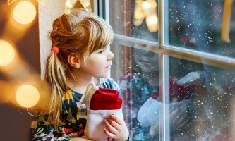 Mädchen sitzt nachdenklich an Fenster mit Weihnachtsbeleuchtung