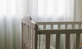 Babybett vor Fenster mit Vorhängen, durch die das Licht fällt 