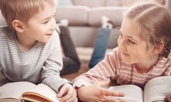 Junge und Mädchen liegen lesend auf dem Boden und lachen sich gegenseitig an 