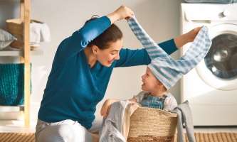 Mutter und Kind albern herum mit Wäsche vor der Waschmaschine