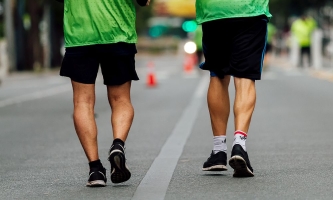 Zwei Männer von hinten joggen über Straße mit Laufschuhen und grünen Warnwesten 