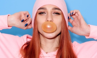 Jugendliche mit roten Haaren und rosa Outfit bläst Kaugummi vor dem Mund auf