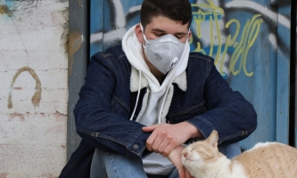 Jugendlicher mit Maske streichelt Katze 