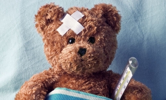 Kranker Teddybär mit Pflaster und Thermometer im Bett