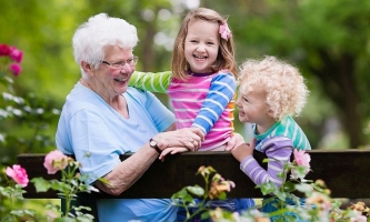 Fröhliche Oma mit Enkeltöchtern auf Gartenbank 