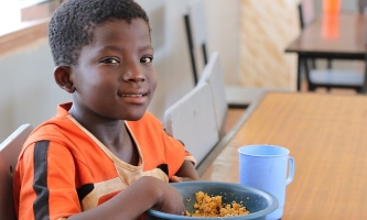 Junge sitzt bei Don Bosco in Ghana am Tisch und isst