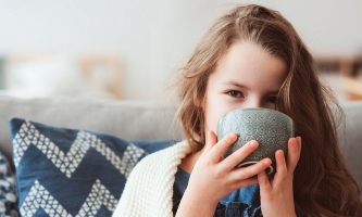 Mädchen auf Sofa mit Decke trinkt Tee