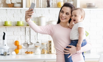 Mutter macht Selfie von sich mit Baby auf dem Arm