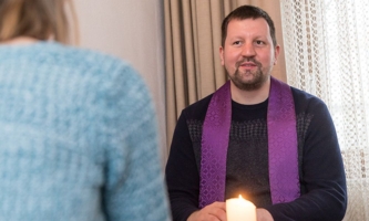 Beichtgespräch zwischen Pfarrer und Frau an Tisch mit Kerze 