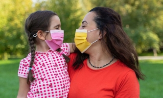 Mutter und Tochter lachend mit Maske auf Wiese 