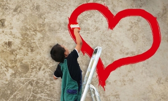 Kind malt mit roter Farbe Herz an Wand 