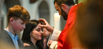 Priester zeichnet einer Jugendlichen mit Chrisamöl ein Kreuz auf die Stirn
